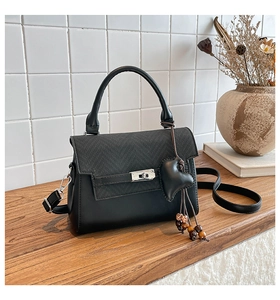 Detail of crossbody bag with silver twist lock and heart charm on a wooden desk