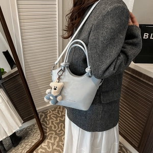 Detail of light blue bucket bag with plush bear charm and wavy edge held by model