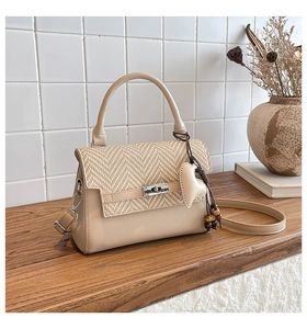 Detail of crossbody bag with straw weave flap, heart pendant, and metal twist lock