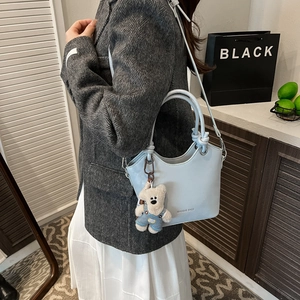 Detail of light blue bucket bag with knotted handle and cute plush bear accessory