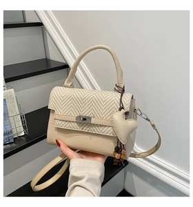 Detail of beige tote bag with herringbone weave flap and heart-shaped leather charm