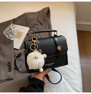 Detail of black leather handbag with white stitching, gold clasp, and plush monster charm