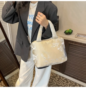 Détails du sac cabas en satin doré avec broderie florale blanche et pendentif à pompon
