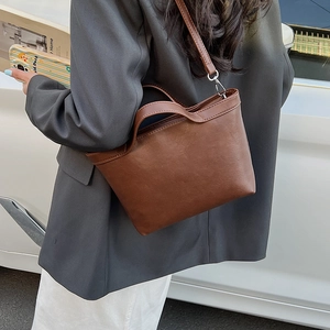 Side view of dark brown leather tote bag with shoulder strap worn on casual grey suit