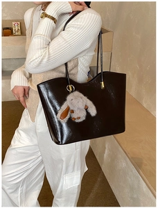 Détail du sac cabas brillant marron foncé avec breloque lapin en peluche porté à l'épaule