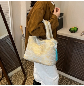 Détail du sac cabas en jacquard blanc aux motifs dorés avec pendentif pompon bleu