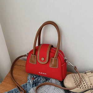 Detail of red canvas crossbody bag with brown leather handles and adjustable strap