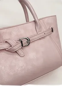 Detail of light pink leather handbag with refined pebble texture and silver buckle