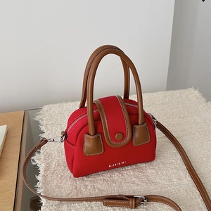 Detail view of red fabric mini Boston bag with brown leather trim on soft white cushion