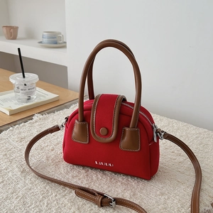 Detail of red canvas crossbody bag with brown leather trim and white stitching accents