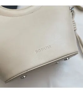 Détail d'un sac seau en cuir beige avec gaufrage NO FILTER et pieds en métal
