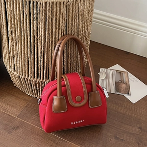 Detail of red canvas handbag featuring brown leather handles and embroidered logo