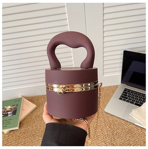 Detail of burgundy cylindrical clutch bag with golden spherical clasp and metal chain