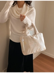 Détail du sac cabas en satin champagne avec broderie florale et breloque à pompon blanc