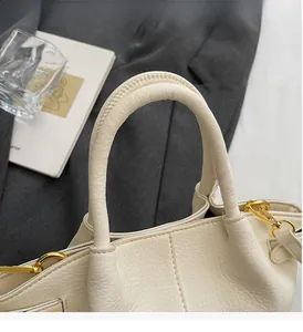 Détail d'un sac à main en cuir grainé beige avec poignées cylindriques et boucles dorées