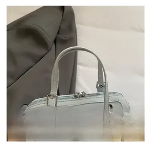 Detail of light blue pillow bag with metal zipper, smooth handle and plush ball charm