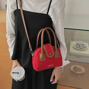 Detail of red canvas crossbody bag with brown leather handles and adjustable shoulder strap