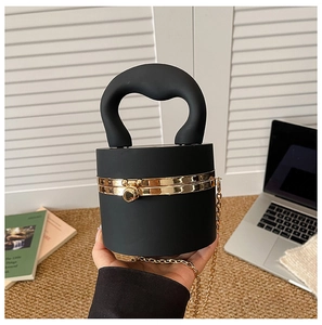 Detail of a matte black cylindrical clutch bag featuring golden metal hardware and circular clasp