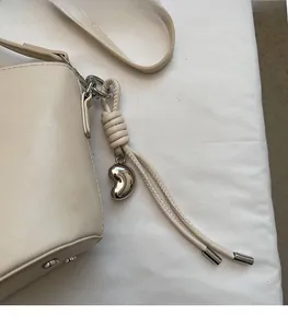 Détail du sac seau en PU crème avec pendentif nœud tissé et breloque en métal argenté