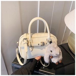 Detail of off-white leather handbag with pebbled texture and plush rabbit keychain