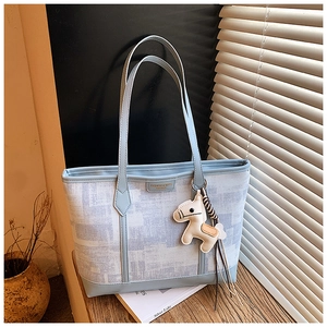 Detail of light blue tote bag with geometric pattern and horse-shaped charm on wooden table