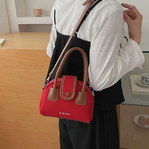 Detail shot of the red textured fabric and brown leather handle on a chic crossbody bag
