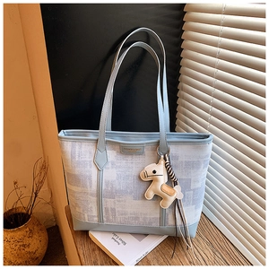 Detail of light blue printed tote bag with a small horse charm on a wooden table