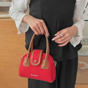 Close-up of red canvas handbag with leather handle and white stitching details