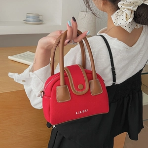 Red canvas crossbody bag with brown leather handles worn with a white shirt and black dress