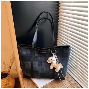 Detail of denim tote bag with leather trim and beige horse charm on wooden table