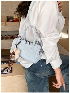Light blue Boston bag with denim teddy bear charm shown in a street style setting