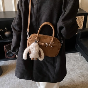 Detail of caramel leather crossbody bag with metal buckle and plush bunny charm