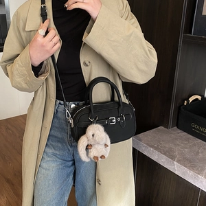 Detail of a black crossbody bag with silver buckle and grey plush rabbit charm on a model