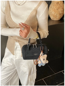 Detail of black Boston bag featuring dual handles and a cute plush bear charm accessory