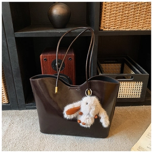 Détail d'un sac cabas rétro en cuir marron foncé avec un porte-clé lapin en peluche