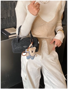 Detail of black leather cylinder bag with cute bear charm and white fashion text logo