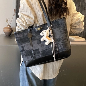 Detail of grey textured tote bag with black leather base and white horse charm accessory