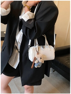 White Boston pillow bag with plush bear charm worn as crossbody on a black blazer
