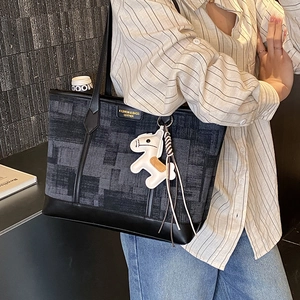 Detail of a large black leather and blue plaid tote bag with a white horse charm