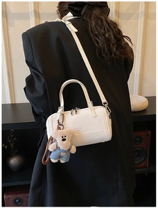 Detail of a beige leather Boston bag with a cute plush bear charm on a model