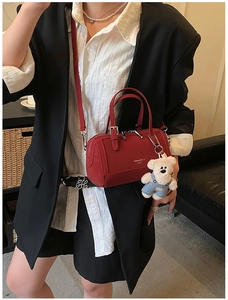 Detail of red leather Boston bag featuring a white plush bear charm and crossbody strap