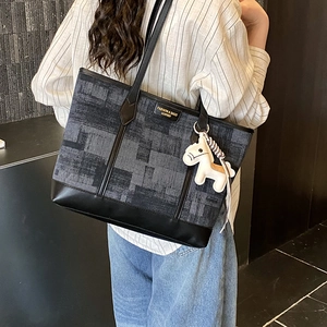 Macro view of a large grey checkered tote bag with leather trim and horse charm