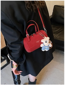 Red leather Boston bag with teddy bear charm shown as crossbody on black blazer
