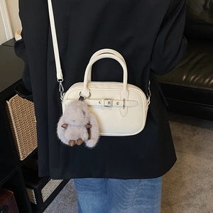 Detail of cream crossbody bag with leather buckle and plush bunny charm on black blazer