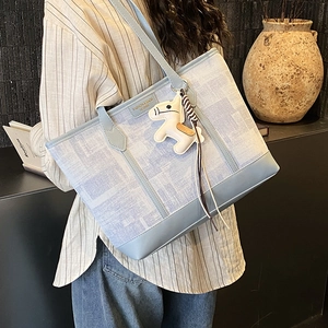 Detail of light blue textured canvas tote bag with leather trim and horse charm