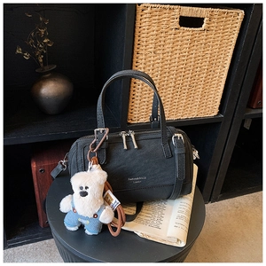 Detail of black leather Boston bag with a cute bear charm on a dark display stand