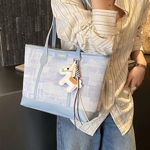 Blue plaid tote bag with leather handles and horse charm, worn by model on shoulder
