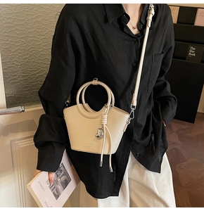 Detail view of cream bucket bag with curved rim, round handle and heart charm pendant