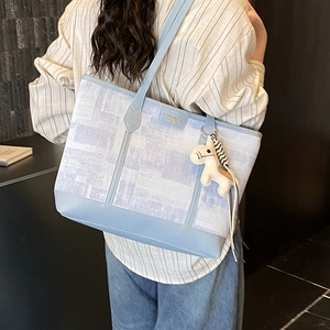 Detail of blue and white tote bag with purple prints and white horse pendant on a model