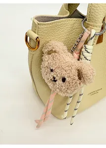 Détail d'un porte-clés ours en peluche marron avec cordons sur un sac seau en cuir grainé